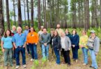 A group of attendees stand for a photo in fronta line of trees.