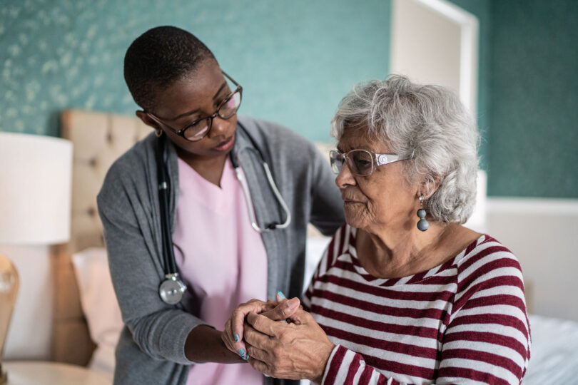 A health care provider holds the hand of an older patient.